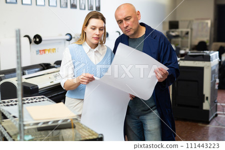Service engineer and office worker checking printed document together against color chart closeup 111443223