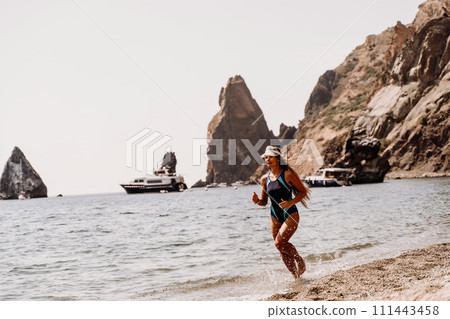 Woman beach vacation photo. A happy tourist in a blue bikini enjoying the scenic view of the sea and volcanic mountains while taking pictures to capture the memories of her travel adventure. Woman beach vacation photo. A happy tourist in a blue bikini enjoying the scenic view of the sea and volcanic mountains while taking pictures to capture the memories of her travel adventure. 111443458
