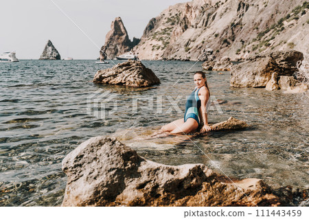 Woman beach vacation photo. A happy tourist in a blue bikini enjoying the scenic view of the sea and volcanic mountains while taking pictures to capture the memories of her travel adventure. 111443459