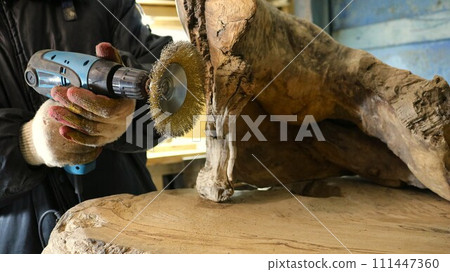 processing wood with a sander with a metal round bristle disk in a carpenter's workshop, sanding a piece of solid wood in the process of producing wooden carpentry processing wood with a sander with a metal round bristle disk in a carpenter's workshop, sanding a piece of solid wood in the process of producing wooden carpentry 111447360