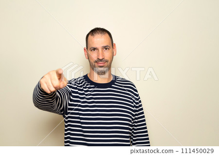 Portrait of handsome man in his 40s pointing index finger at you over isolated beige background, looking at camera. A friendly, smiling guy pointing his index finger at the camera choosing you 111450029
