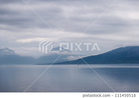 A lone sailboat in vast Norwegian fjord, shrouded peaks loom 111450518