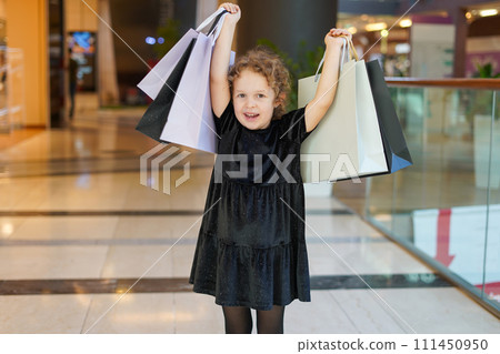 Happy child girl in black dress on shopping. kid with shopping bags. Black Friday concept Happy child girl in black dress on shopping. kid with shopping bags. Black Friday concept 111450950