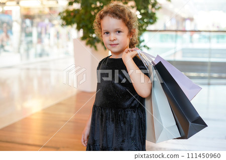 cute child girl in black dress on shopping. portrait of a kid with shopping bags. Black Friday concept cute child girl in black dress on shopping. portrait of a kid with shopping bags. Black Friday concept 111450960