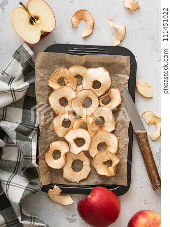 Sweet dried apple rings on baking tray with knife and kitchen towel. 111451022