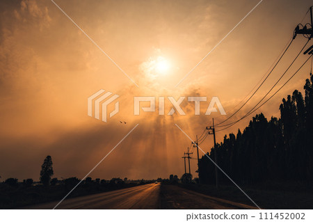Golden sunset sky with sunbeam over rural road and eletricity pole in countryside Golden sunset sky with sunbeam over rural road and eletricity pole in countryside 111452002