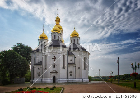 The ancient Orthodox Church of St. Catherine, a resplendent white church with gilded domes and crosses, as it stands against the serene blue sky with soft, billowing clouds. The ancient Orthodox Church of St. Catherine, a resplendent white church with gilded domes and crosses, as it stands against the serene blue sky with soft, billowing clouds. 111452596