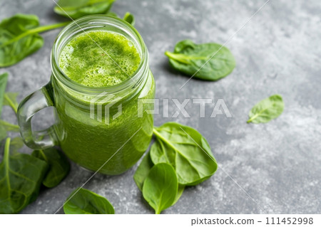 Green detox smoothie in a jar surrounded by basil leaves on a grey background with space for text 111452998