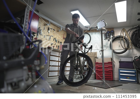 A man is fixing a bicycle in a garage A man is fixing a bicycle in a garage 111453395