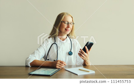 woman doctor using phone with documents, digital tablet computer sitting at desk in clinic office woman doctor using phone with documents, digital tablet computer sitting at desk in clinic office 111455753