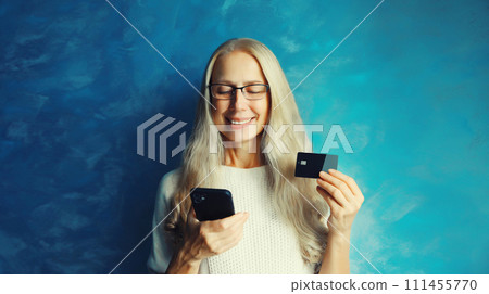 happy middle aged woman shopping online looking at mobile phone holding plastic credit bank card i 111455770
