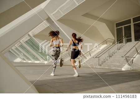 Back view of sporty female friends in sportswear running outdoors on a sunny day . Morning jog 111456183