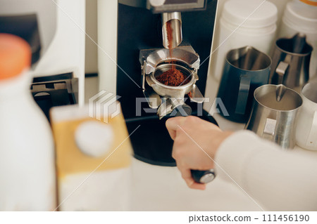 Close up of female barista grinding coffee using professional grinder machine in coffee house 111456190
