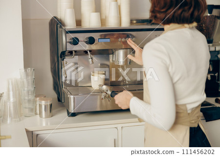 Back view of female barista making coffee in a coffee machine while working in cafe Back view of female barista making coffee in a coffee machine while working in cafe 111456202