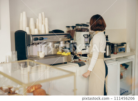 Professional female barista grind coffee bean with grinder machine while working in cafe Professional female barista grind coffee bean with grinder machine while working in cafe 111456206