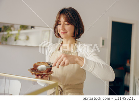 Pretty female waitress hands putting a delicious dessert on a plate standing behind bar counter 111456213