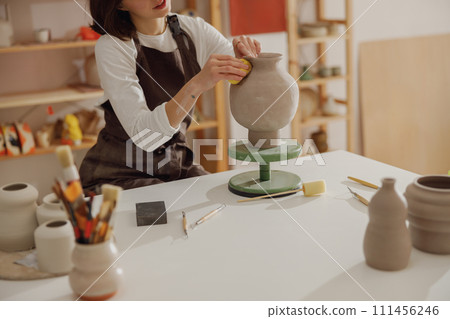 Close up of young female ceramist wearing apron work with unfired clay vase in pottery studio 111456246