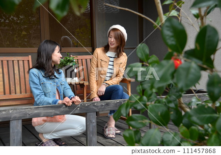 兩個年輕女子在女孩旅行時入住的旅館房間的露臺上一邊看著花園一邊聊天。 兩個年輕女子在女孩旅行時入住的旅館房間的露臺上一邊看著花園一邊聊天。 111457868