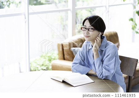 A middle-aged woman reading a book while listening to music in the living room 111461935