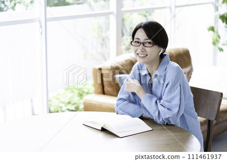 A middle-aged woman reading a book while listening to music in the living room 111461937