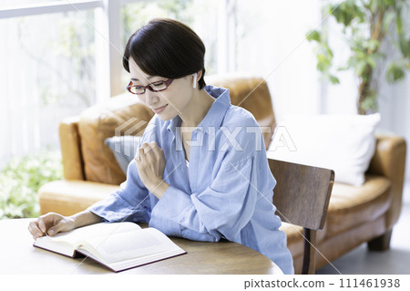 A middle-aged woman reading a book while listening to music in the living room 111461938