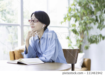 A middle-aged woman reading a book while listening to music in the living room A middle-aged woman reading a book while listening to music in the living room 111461942