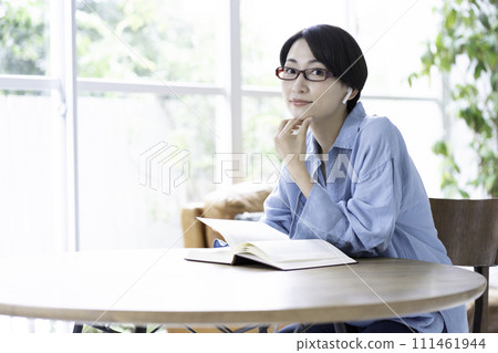 A middle-aged woman reading a book while listening to music in the living room A middle-aged woman reading a book while listening to music in the living room 111461944