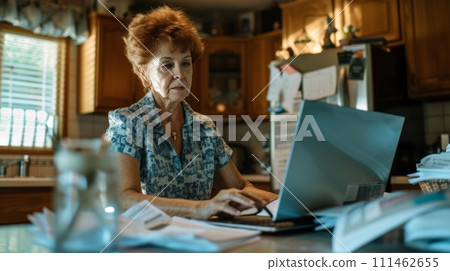 Old woman doing taxes on laptop in a kitchen with document on table 111462655
