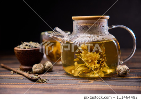 Teapot and glass cup with blooming tea flower inside on a wooden table 111464482