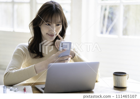 A woman using a smartphone while using a laptop 111465107