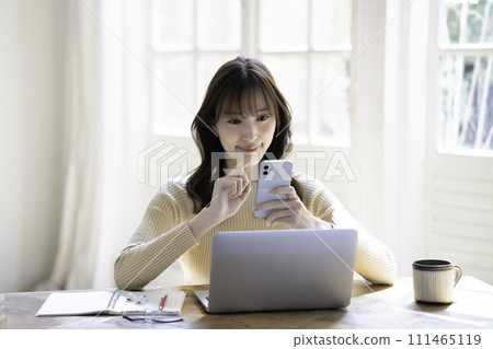 一位女士在使用筆記型電腦時使用智慧型手機 111465119