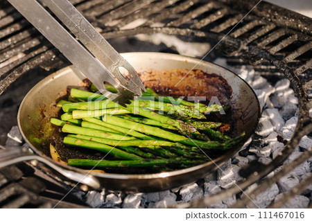 Close-up of healthy frying green asparagus with butter and garlic on carbon steel frying pan. Outdoor BBQ grill Close-up of healthy frying green asparagus with butter and garlic on carbon steel frying pan. Outdoor BBQ grill 111467016