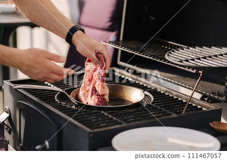 Male hand put T-bone Steak on a heated pan. Man grilling steak on carbon steel pan. French cuisine. BBQ concept 111467057