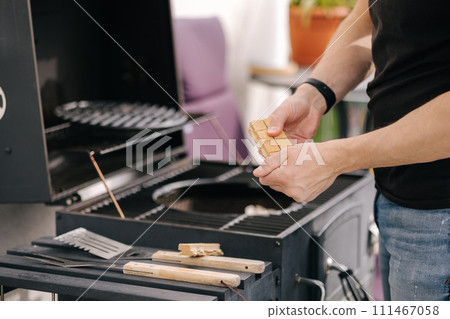 Close-up of man use fire briquettes for lighting a fire in the grill. Outdoor barbecue on terrace Close-up of man use fire briquettes for lighting a fire in the grill. Outdoor barbecue on terrace 111467058