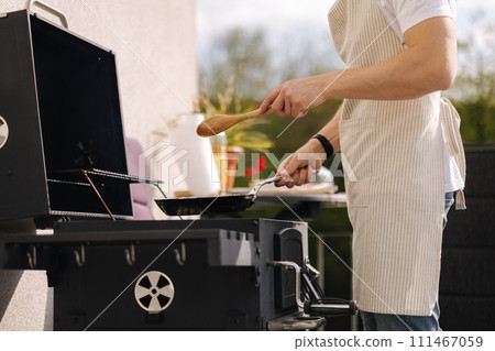 Middle selection of man in apron using wooden spoon to mix vegetables on frying pan. Prepare food on grill 111467059