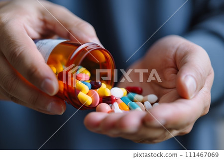 Close up view of a hand pouring a variety of pills from a bottle into the palm of his hand 111467069