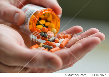 Close up view of a hand pouring a variety of pills from a bottle into the palm of his hand 111467074