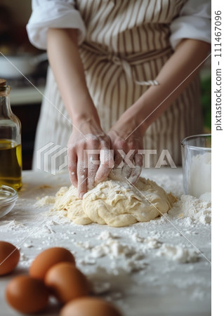 A pair of hands kneading dough in the kitchen on a white table surrounded by ingredients for cooking A pair of hands kneading dough in the kitchen on a white table surrounded by ingredients for cooking 111467096