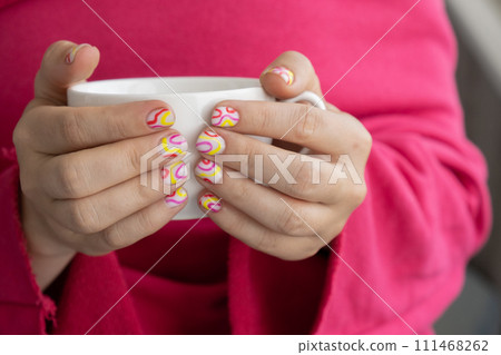 Pastel softness colorful manicured nails. Woman holding white cup of coffee or tea showing her new summer manicure in colors of pastel palette. Simplicity decor fresh spring vibes earth-colored 111468262