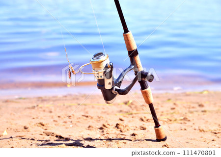 fishing rod with reel on the background of the river, blue water, sun, sand 111470801