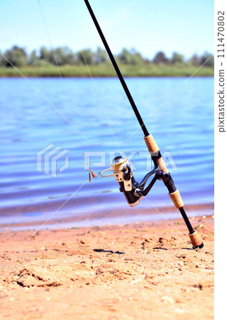fishing rod with reel on the background of the river, blue water, sun, sand 111470802