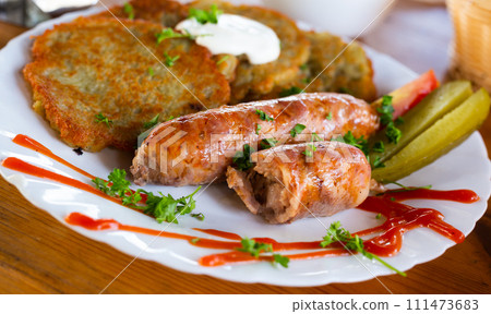 Potato pancakes with fried sausages on a white plate 111473683