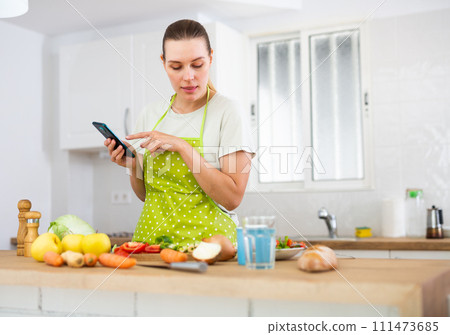 Young woman cooking dinner at home, using smartphone 111473685