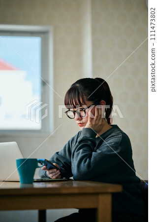 一位年輕女子托著下巴操作智慧型手機 111473802
