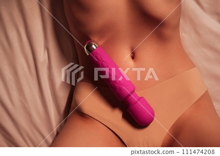 pink vibrator in on female stomach of woman girl with a sexy body in panties lying on bed. Sex toys for female satisfaction and orgasm 111474208
