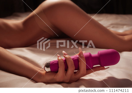 pink sex vibrator in hand of a woman girl with a sexy body and ass in underwear lying on white sheet on bed in bedroom. Sex toys for female satisfaction and orgasm pink sex vibrator in hand of a woman girl with a sexy body and ass in underwear lying on white sheet on bed in bedroom. Sex toys for female satisfaction and orgasm 111474211