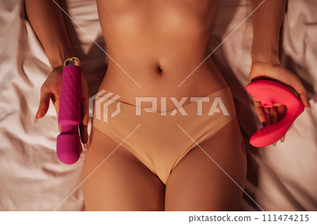 sex vibrator and vacuum stimulator in hands of a naked woman nymphomaniac girl in panties with sexy body lying on bed. Sex toys for female satisfaction and orgasm sex vibrator and vacuum stimulator in hands of a naked woman nymphomaniac girl in panties with sexy body lying on bed. Sex toys for female satisfaction and orgasm 111474215