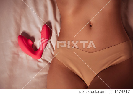 pink vibrator vacuum stimulator lies on a white sheet on bed next to sexy body of girl woman in panties. Female sex toys for satisfaction and orgasm pink vibrator vacuum stimulator lies on a white sheet on bed next to sexy body of girl woman in panties. Female sex toys for satisfaction and orgasm 111474217