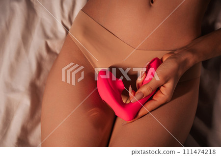 pink vibrator vacuum stimulator in female hand on the stomach of a woman girl with a sexy slender body in panties lying on bed. Sex toys for female satisfaction and orgasm pink vibrator vacuum stimulator in female hand on the stomach of a woman girl with a sexy slender body in panties lying on bed. Sex toys for female satisfaction and orgasm 111474218