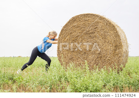 Woman Exercising with Hay Bale in Field 111474924